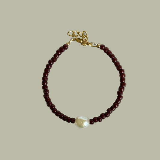 Bracelet with red beads and a pearl on a light gray background