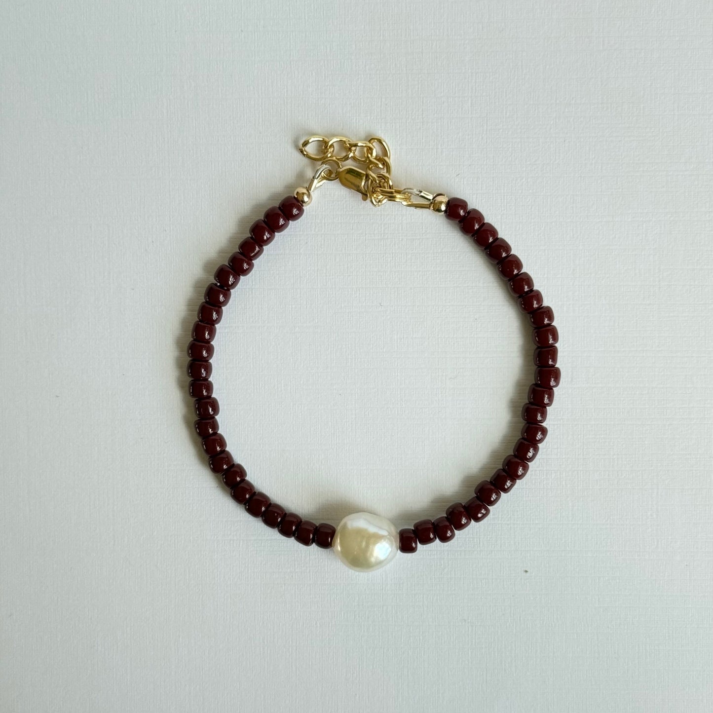 Bracelet with red beads and a pearl on a light gray background