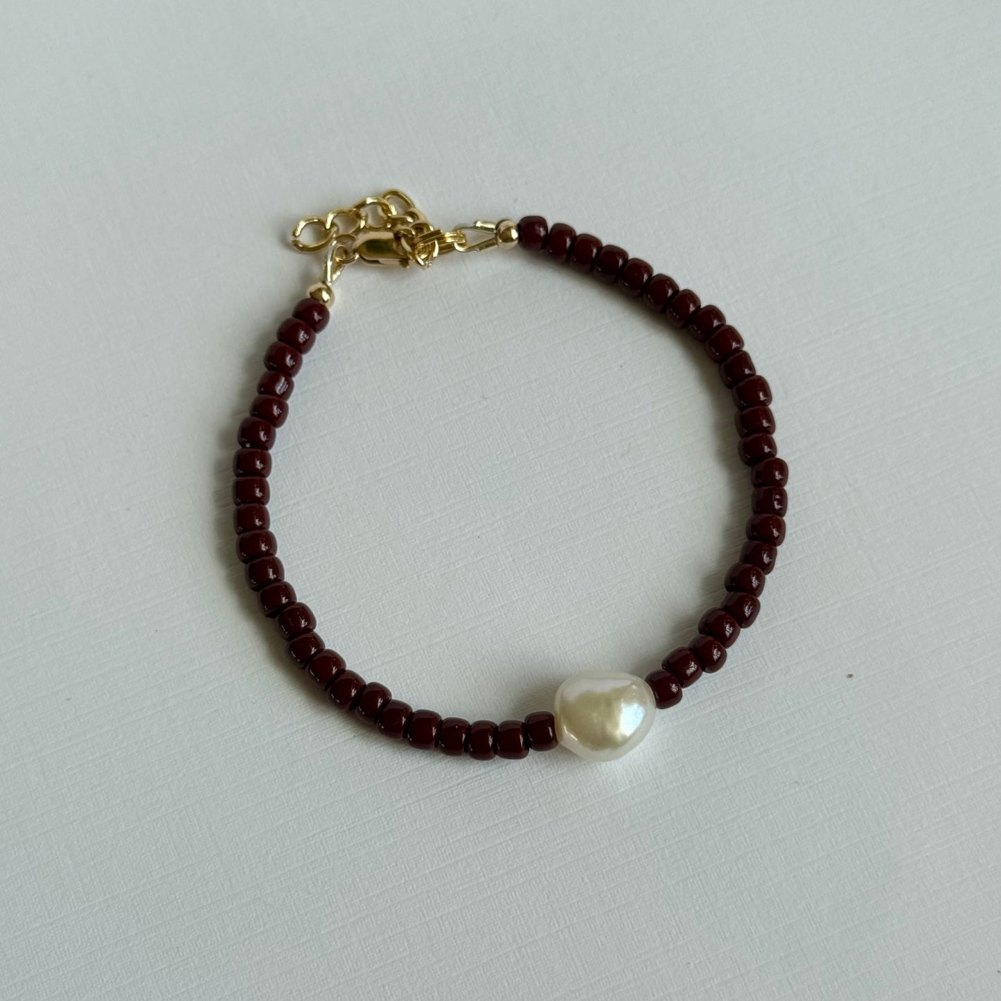 Bracelet with red beads and a pearl on a light gray background