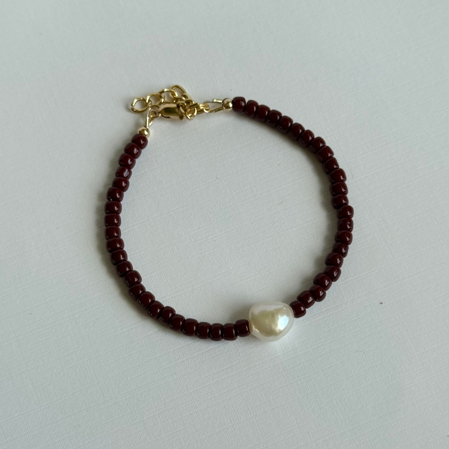 Bracelet with red beads and a pearl on a light gray background