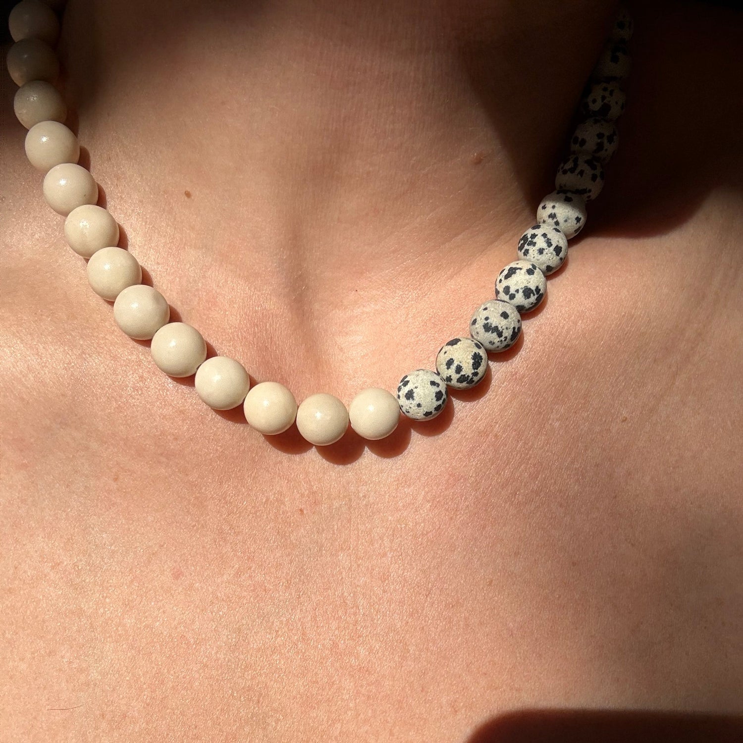 Close-up of a necklace with white beads and black patterns on a person's neck.