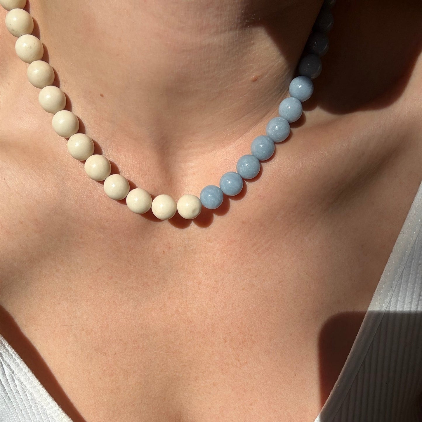 Close-up of a person wearing a white tank top with a necklace featuring blue and white beads.