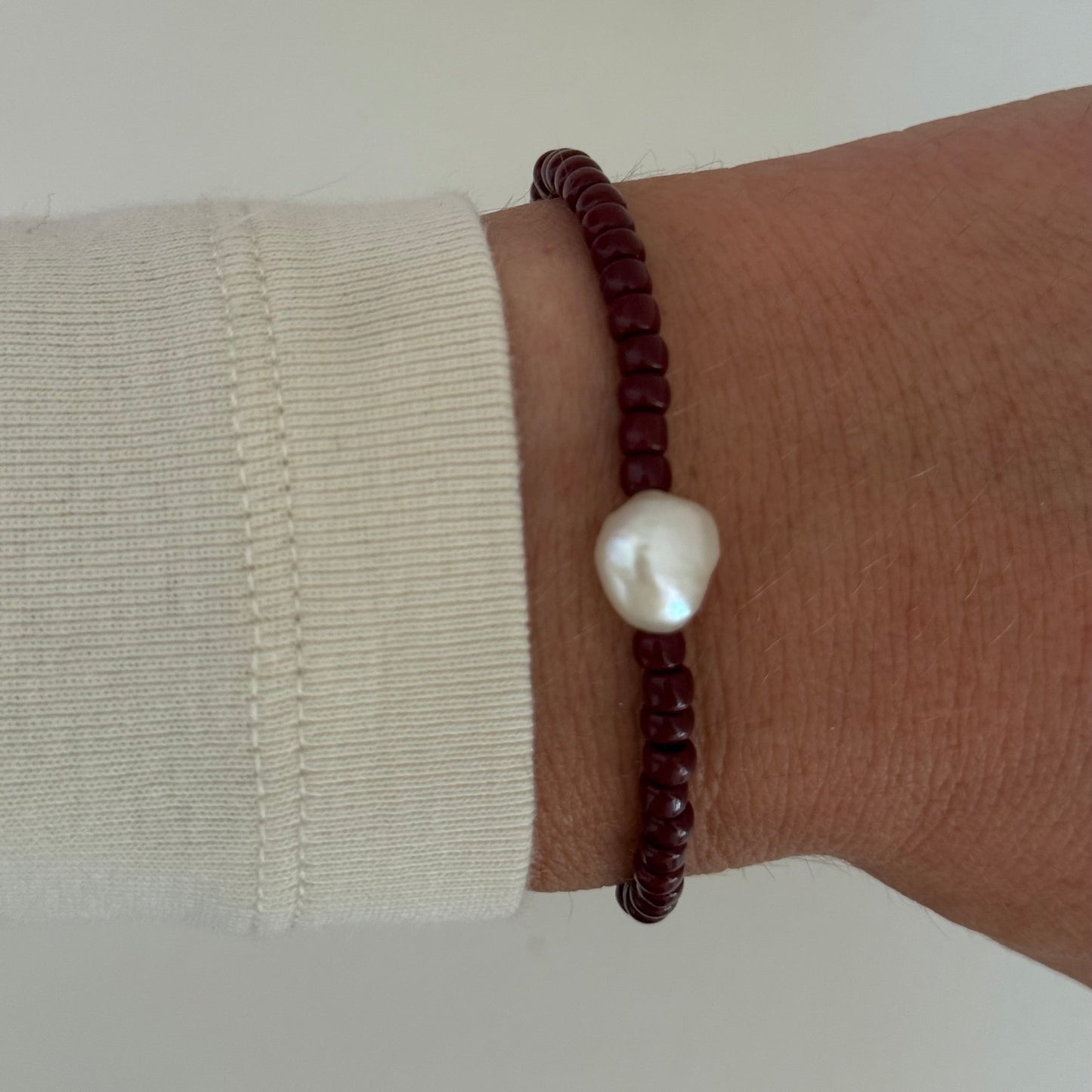 Brown beaded bracelet with a white pearl on a wrist against a neutral background