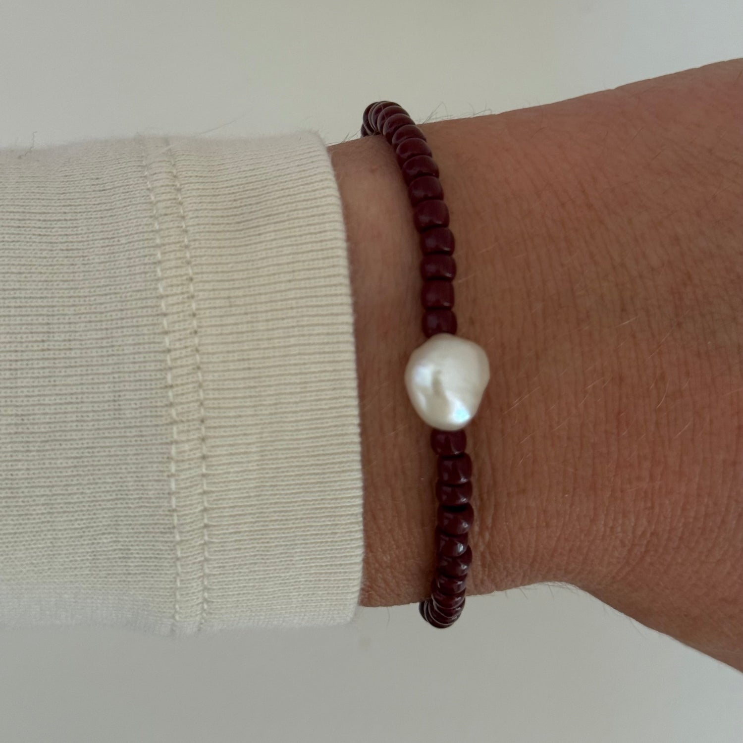 Brown beaded bracelet with a white pearl on a wrist against a neutral background