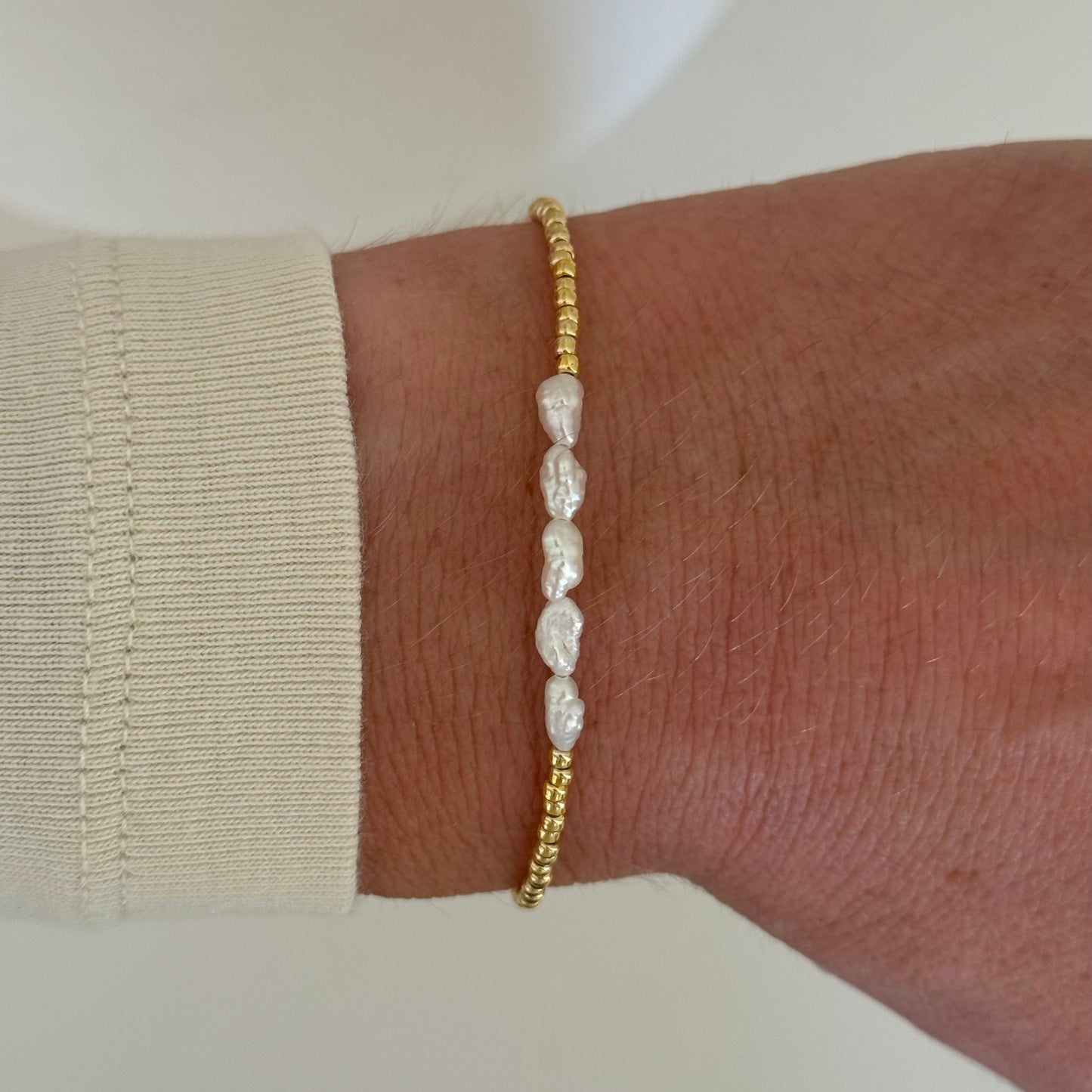 Gold bracelet with pearls on a wrist against a neutral background