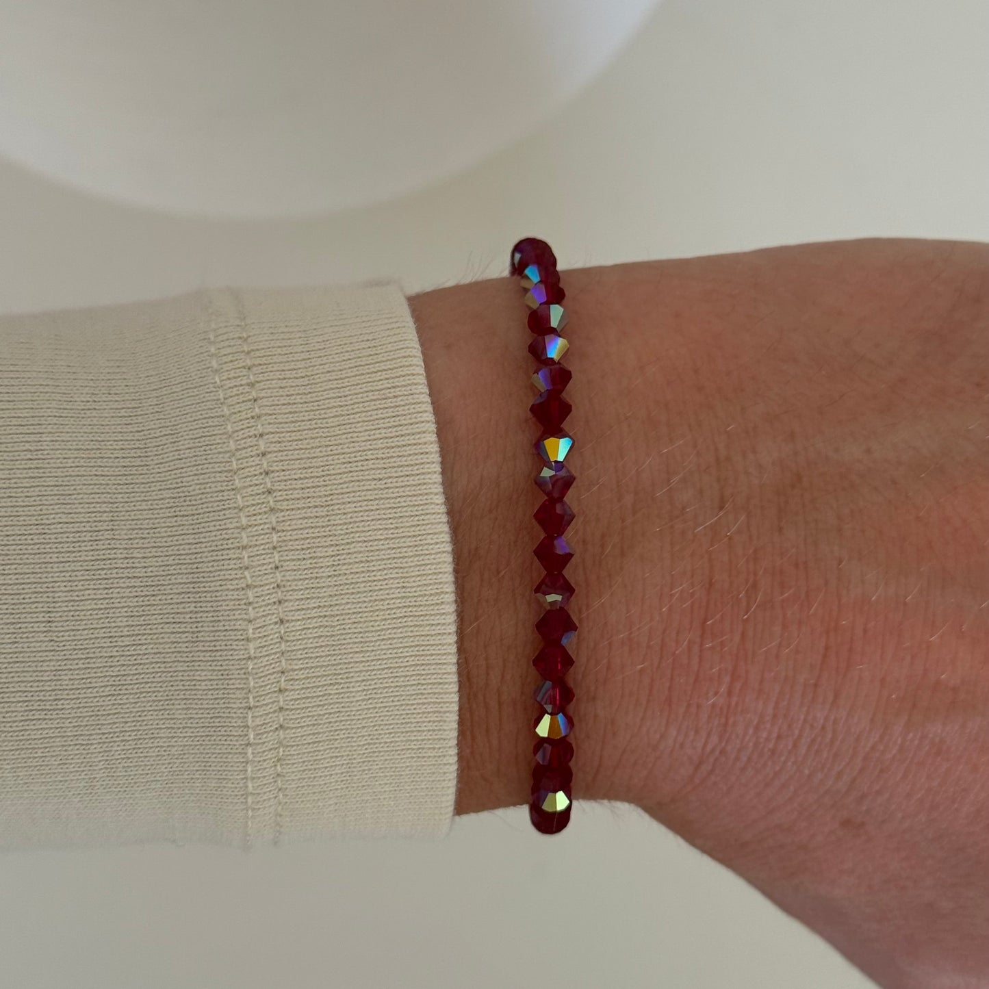 Close-up of a wrist wearing a red beaded bracelet on a neutral background