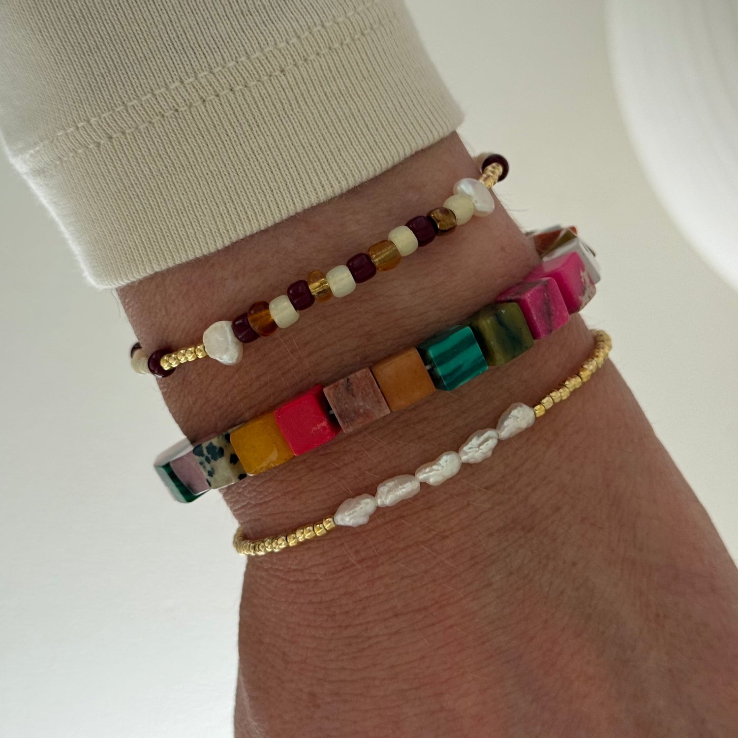 Wrist with multiple colorful beaded bracelets on a plain background