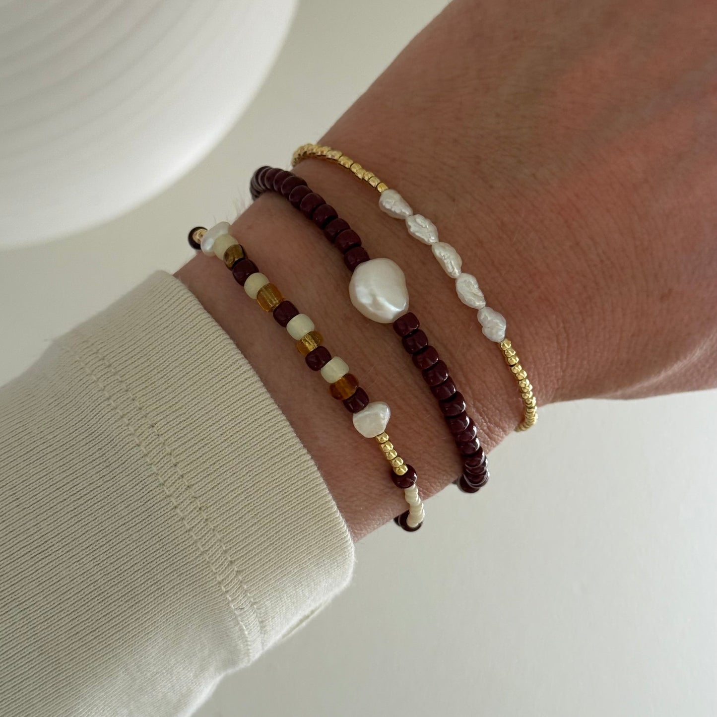 Close-up of a wrist wearing multiple beaded bracelets on a neutral background