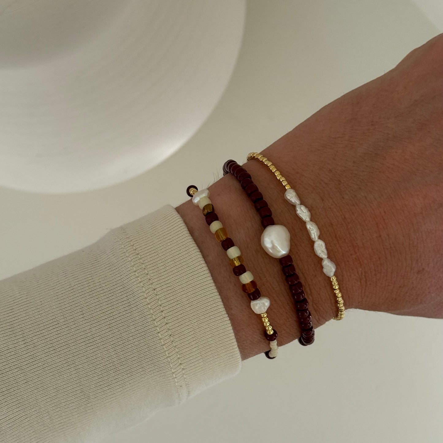 Close-up of a wrist wearing multiple beaded bracelets on a neutral background