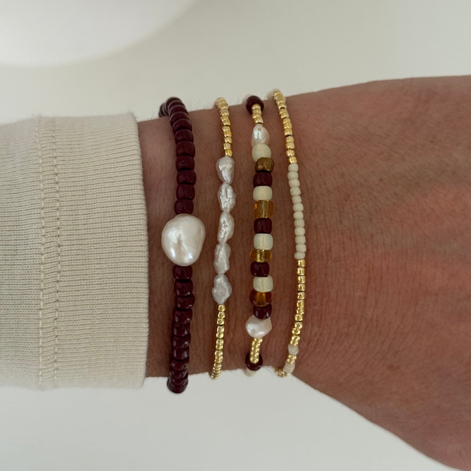 Close-up of a wrist wearing multiple beaded bracelets on a neutral background