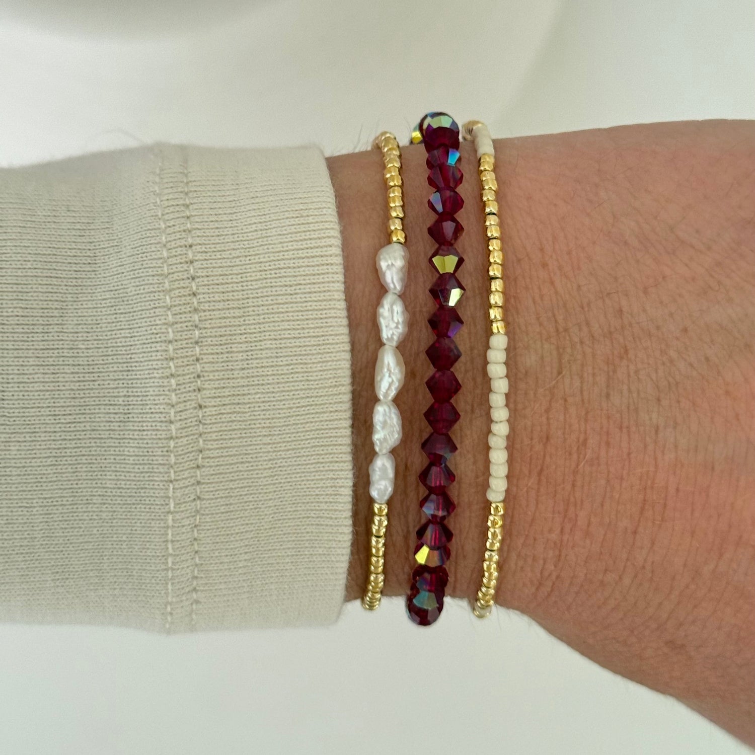 Close-up of a wrist wearing three beaded bracelets on a neutral background