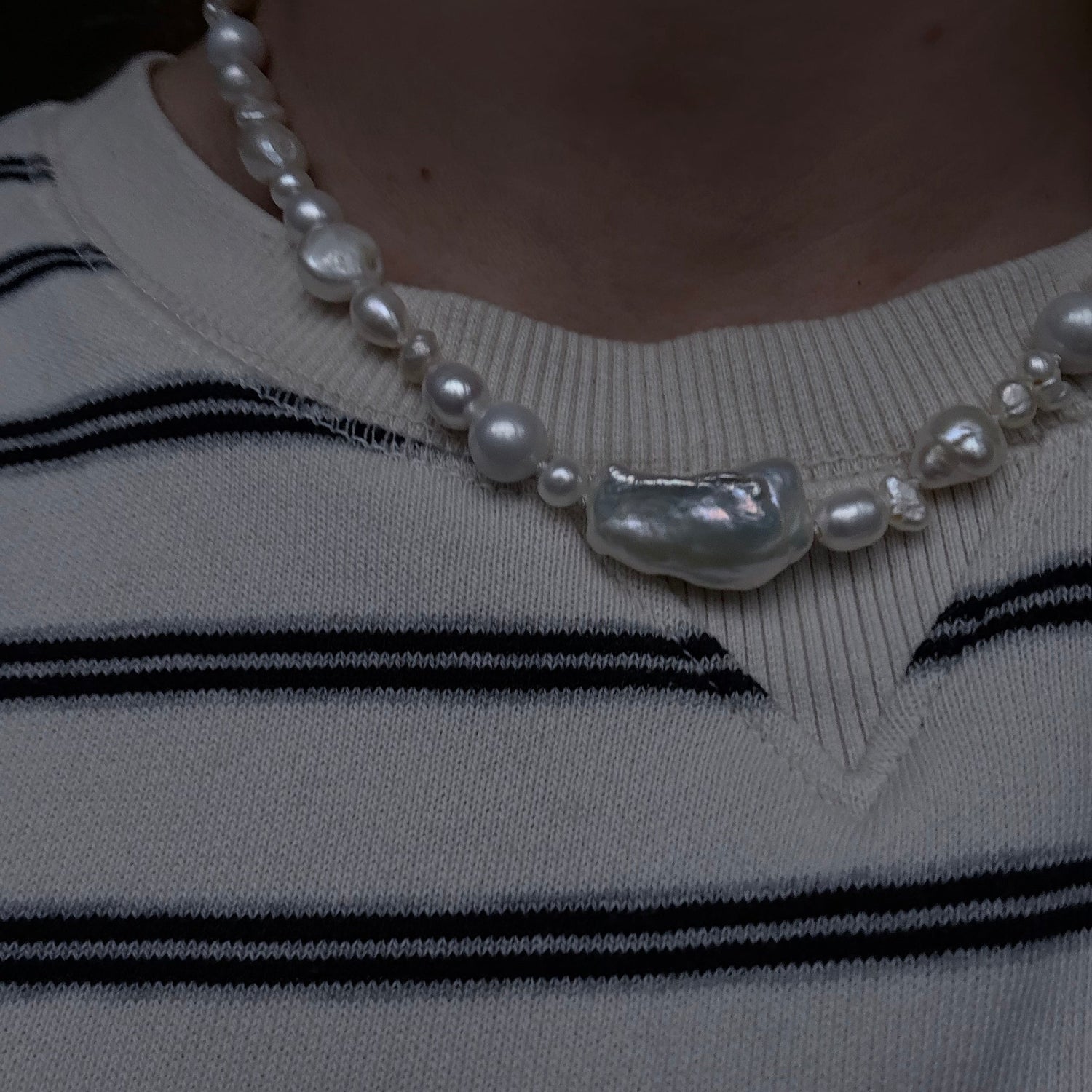 Close-up of a pearl necklace with a decorative clasp on a striped garment.