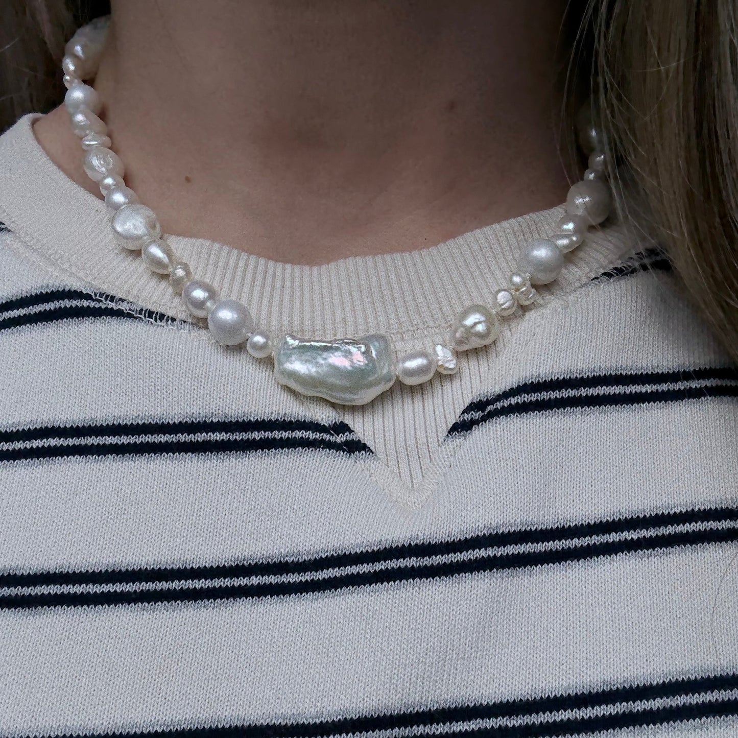 Pearl necklace with a large shell pendant on a person wearing a striped sweater.