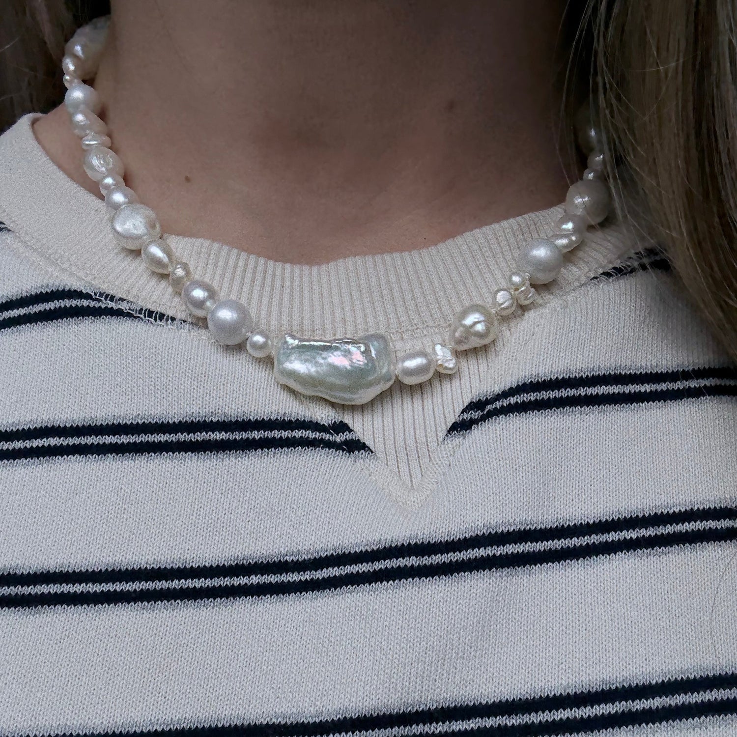Pearl necklace with a large shell pendant on a person wearing a striped sweater.