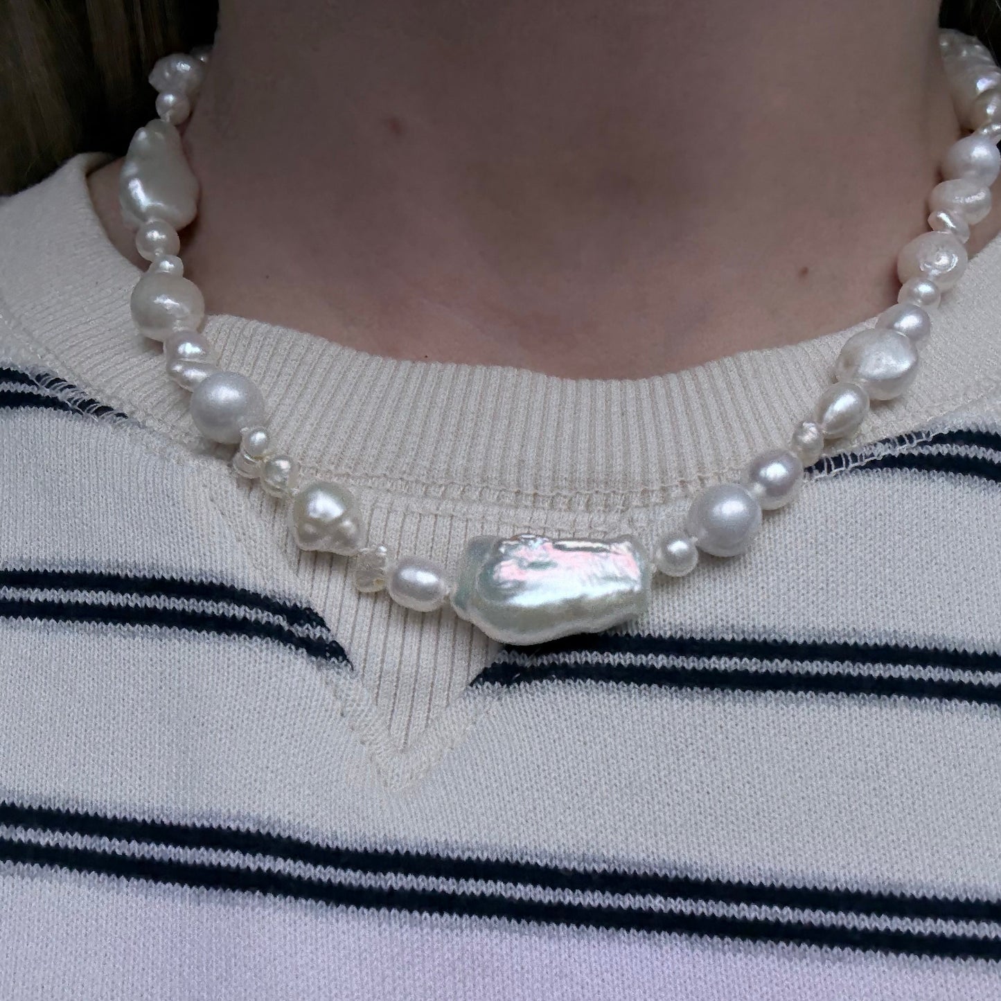 Pearl necklace with a silver clasp on a person wearing a striped sweater.