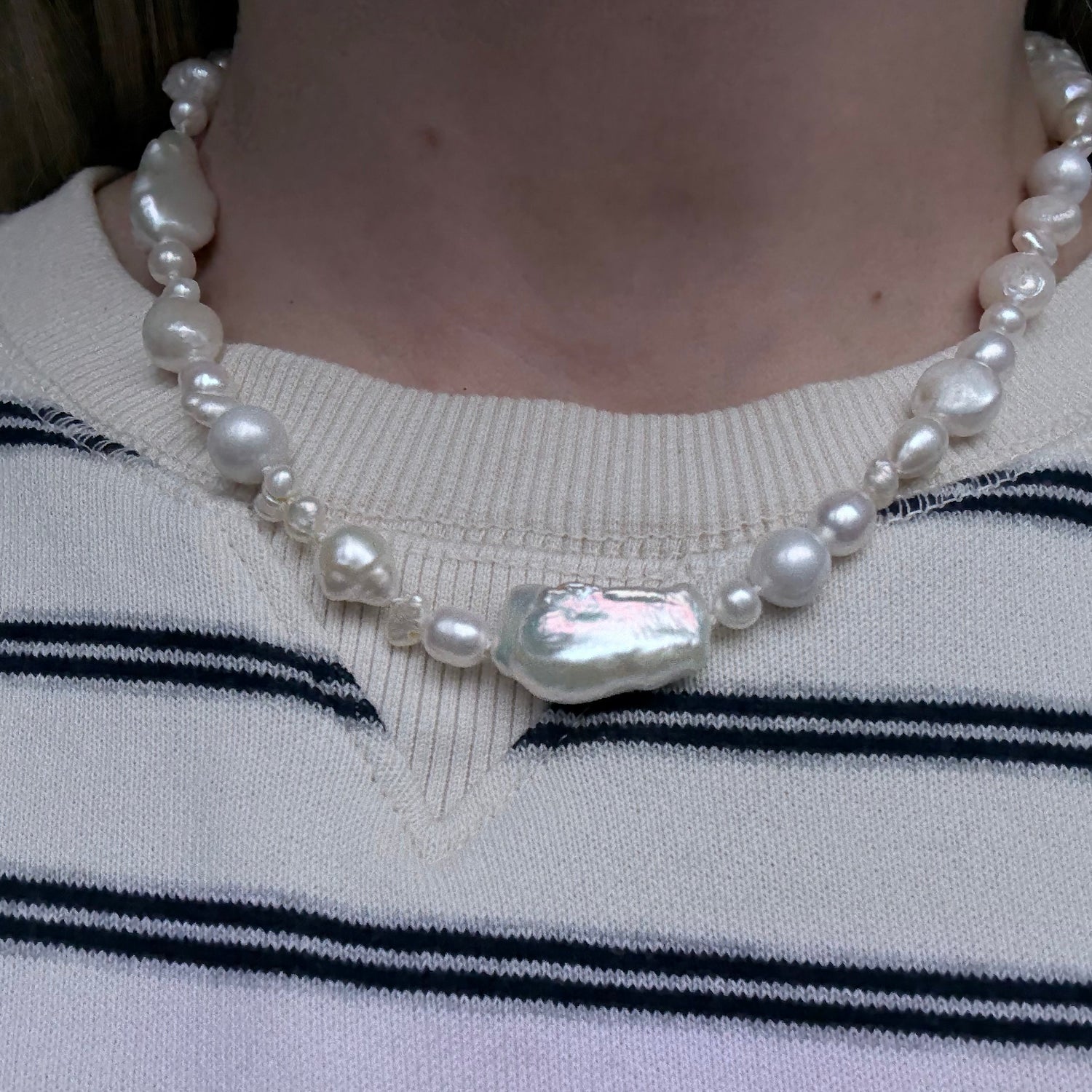 Pearl necklace with a silver clasp on a person wearing a striped sweater.