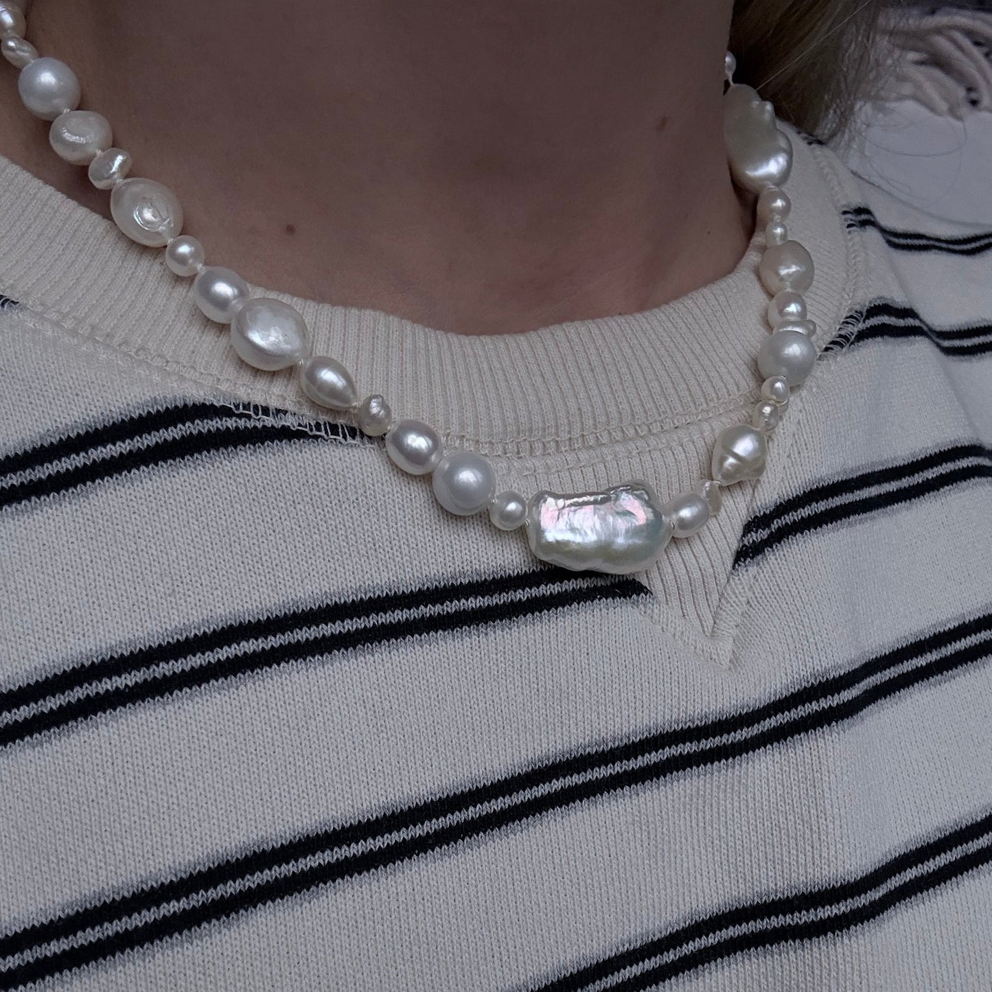 Pearl necklace on a person wearing a white and black striped garment