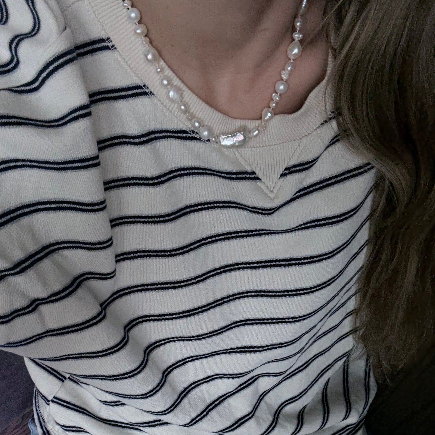 Close-up of a person wearing a striped shirt with a pearl necklace.