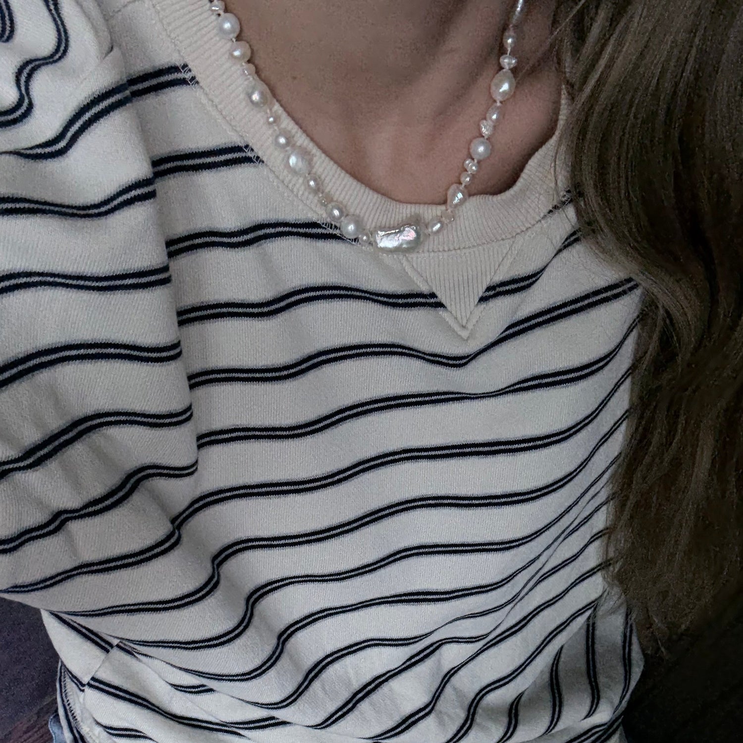 Close-up of a person wearing a striped shirt with a pearl necklace.
