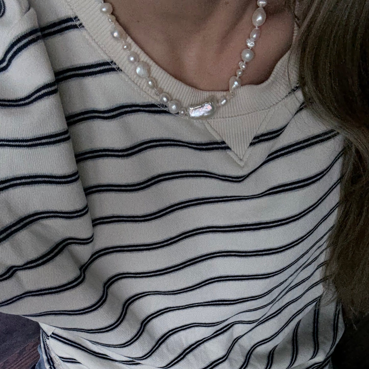 Close-up of a person wearing a striped shirt with a pearl necklace.