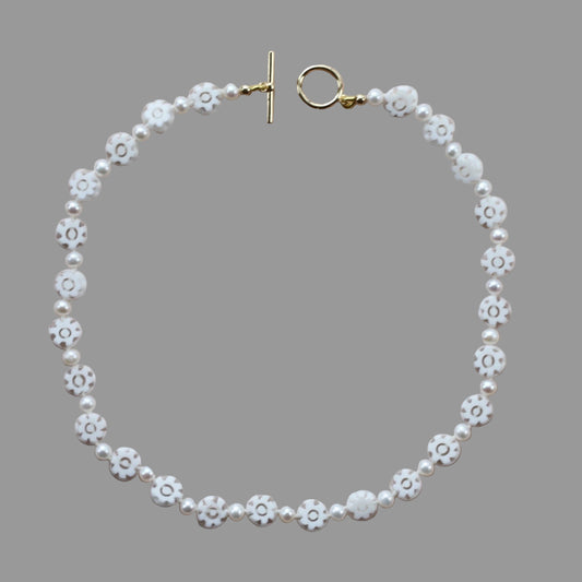 A necklace with white freshwater pearls and gold-colored beads, featuring a gold toggle clasp, displayed against a neutral background.