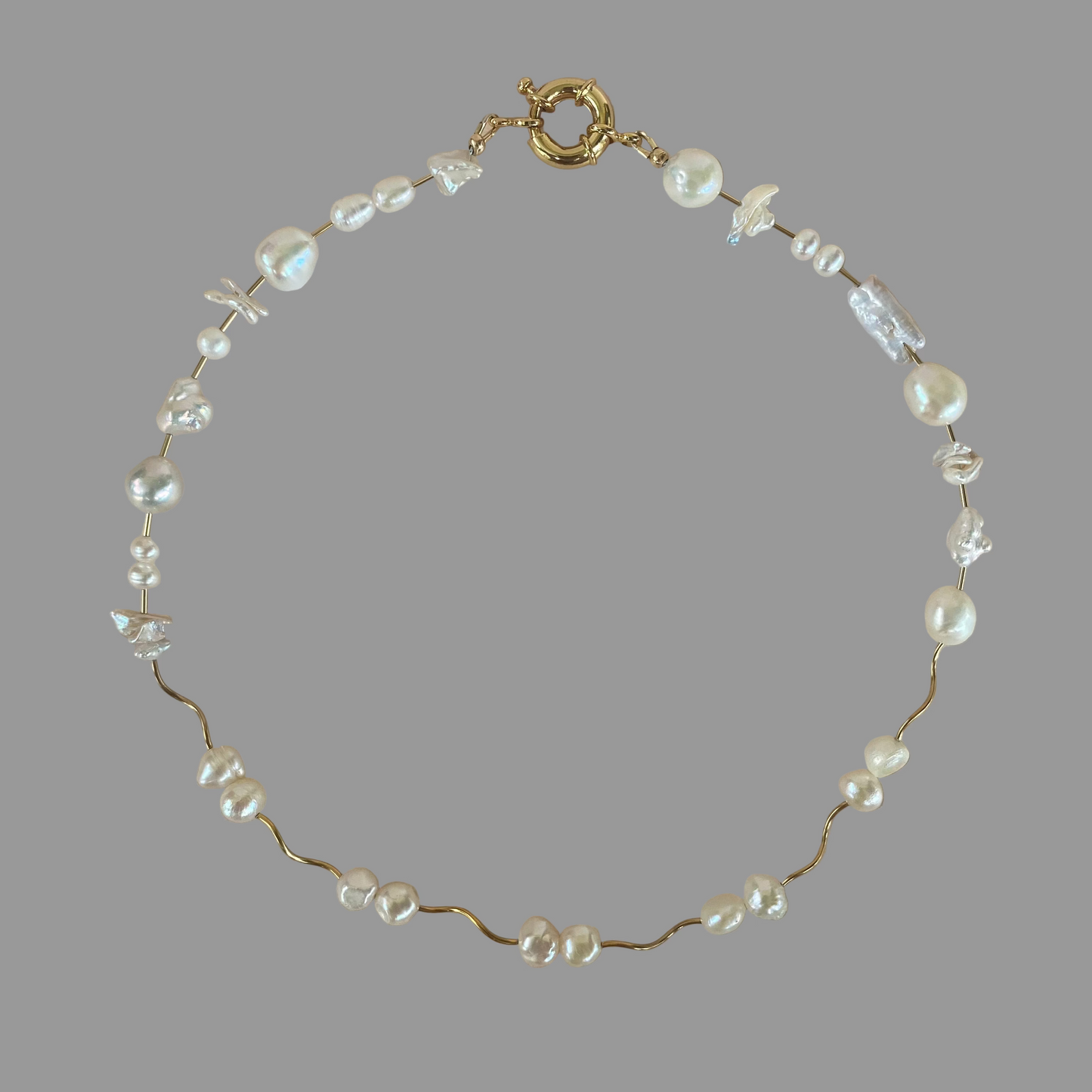A gold-filled necklace featuring a series of freshwater pearls, some of which are baroque and keshi, with a gold-filled tube bead closure.