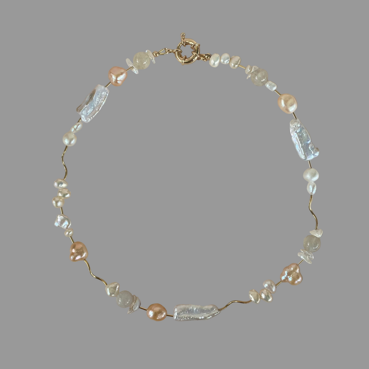 A necklace with a variety of freshwater pearls in different shades of white and peach, interspersed with gold filled tube beads, on a gold filled closure.